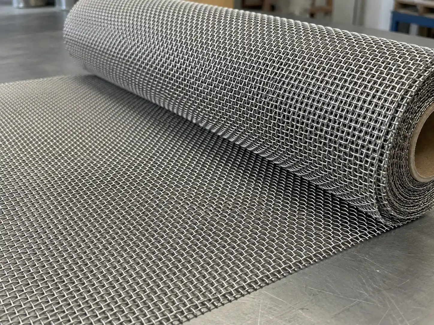 Woven Wire Mesh Woven wire mesh roll displayed on a workshop table with a uniform square opening pattern